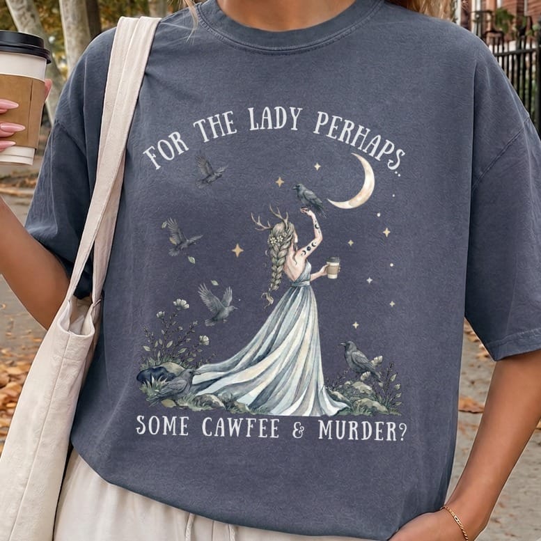 Dark gray t-shirt featuring a graphic of a horned woman surrounded by ravens under a crescent moon and the text FOR THE LADY PERHAPS... SOME CAWFEE & MURDER?