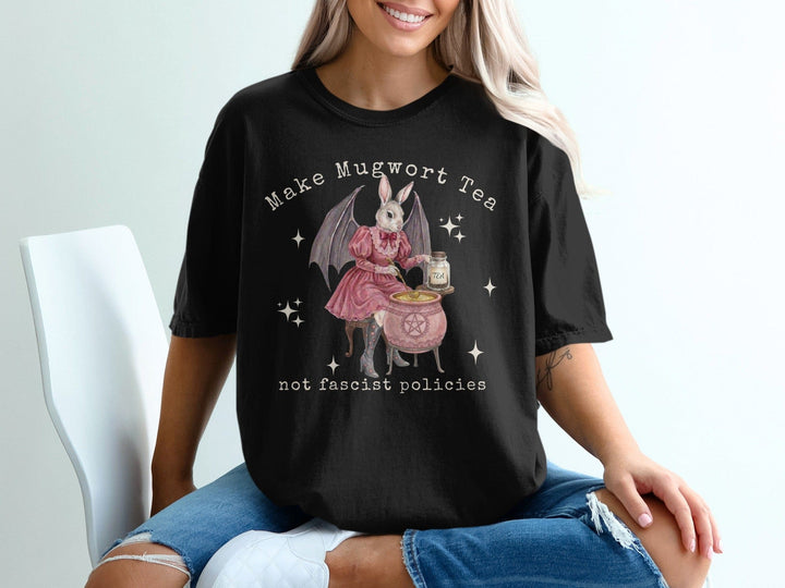 Black t-shirt with a graphic of a rabbit in a witch costume making mugwort tea.