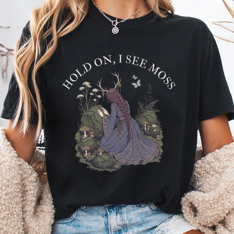 Black t-shirt with "HOLD ON, I SEE MOSS" text and mystical forest graphic.