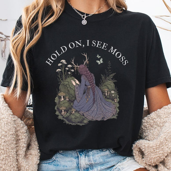 Black t-shirt with "HOLD ON, I SEE MOSS" text and mystical forest graphic.