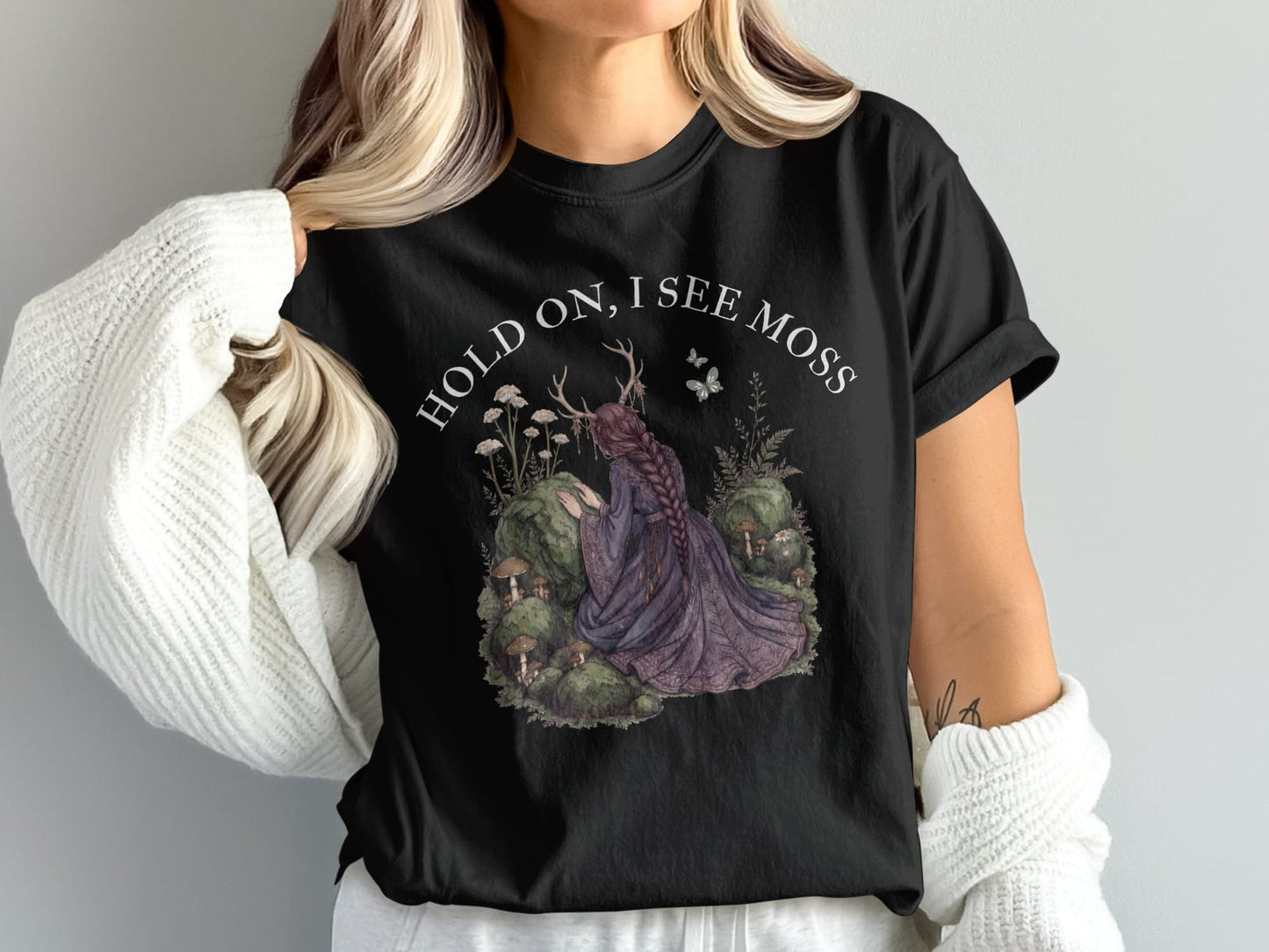 Black t-shirt with text "HOLD ON, I SEE MOSS" and fairy illustration.