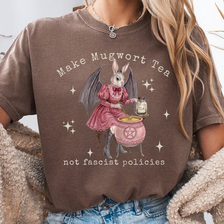 Brown t-shirt with graphic of bunny in dress making mugwort tea, text reads "Make Mugwort Tea not fascist policies".