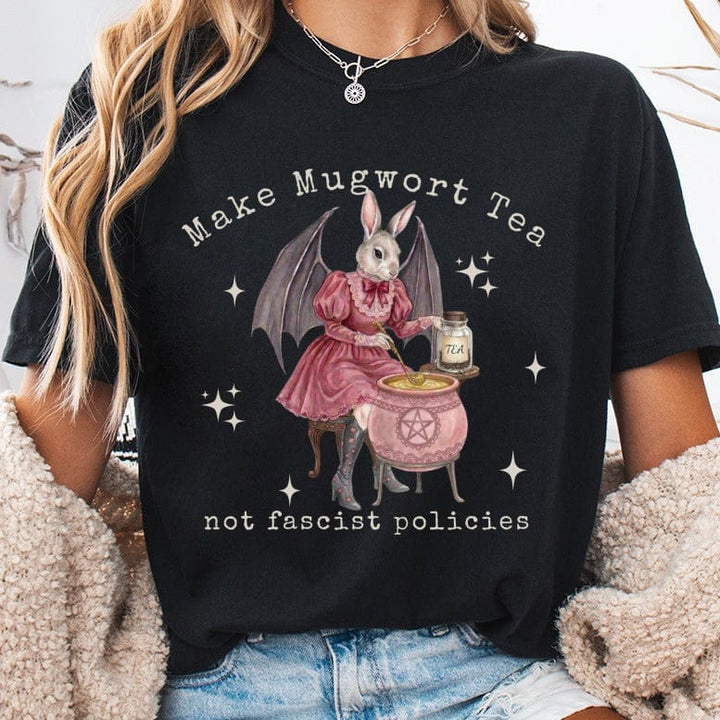 Rabbit in dress brews tea next to cauldron, text "Make Mugwort Tea not fascist policies".