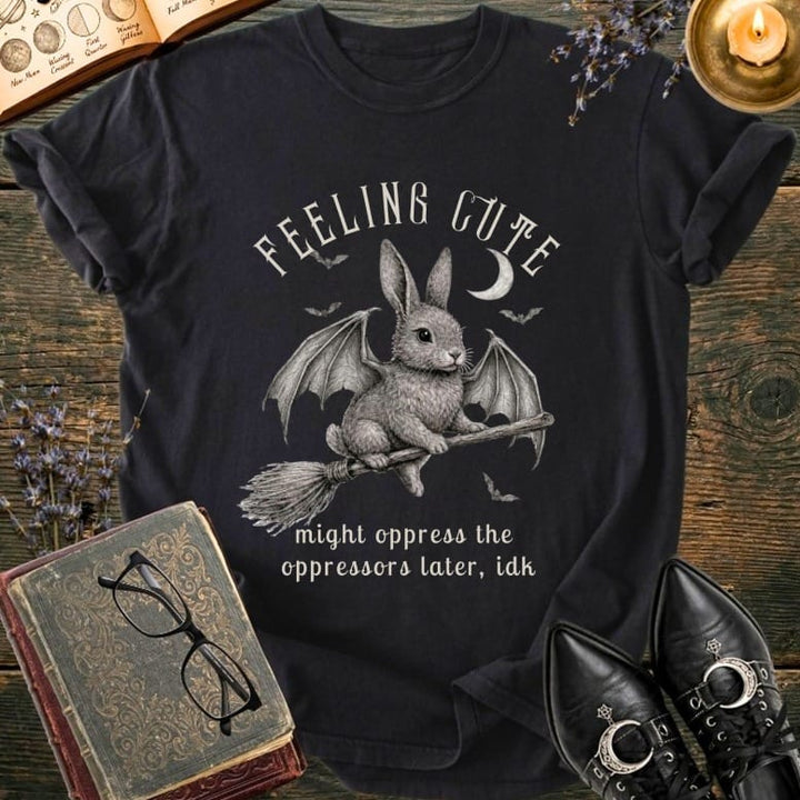 Black t-shirt with a winged bunny on a broom and text "FEELING CUTE might oppress the oppressors later, idk".