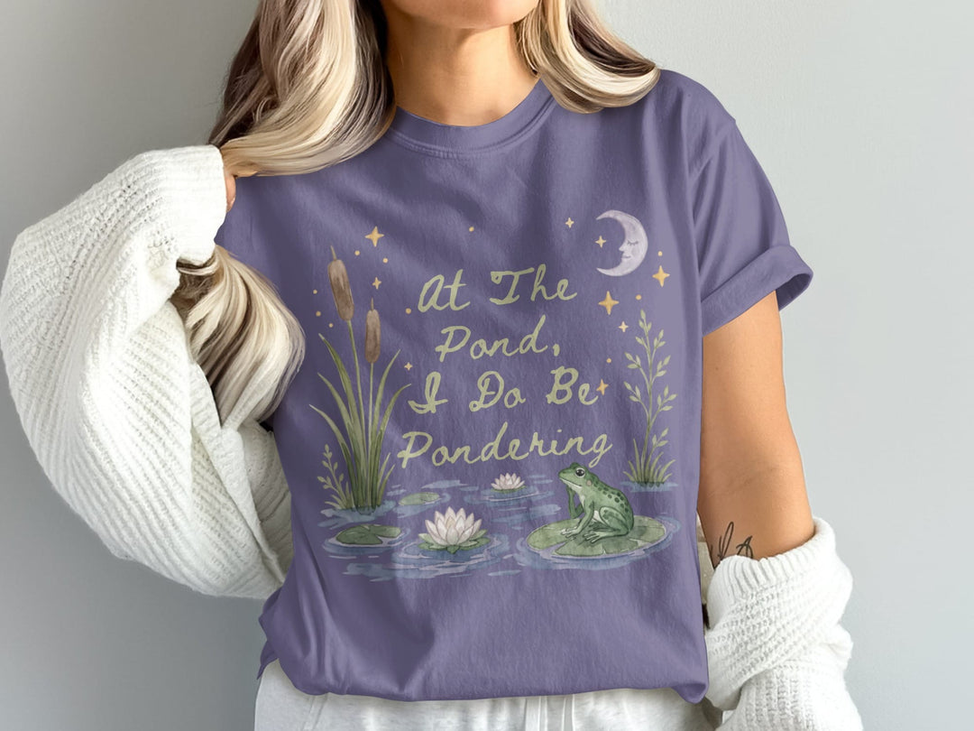 Purple t-shirt with frog, lily pads, cattails, moon, and stars; reads "At The Pond, I Do Bet Pondering".