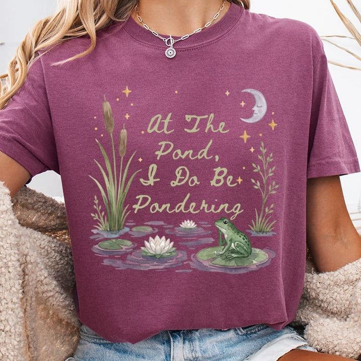 T-shirt with watercolor pond scene, frog, water lilies, and text "At The Pond, I Do Be Pondering".