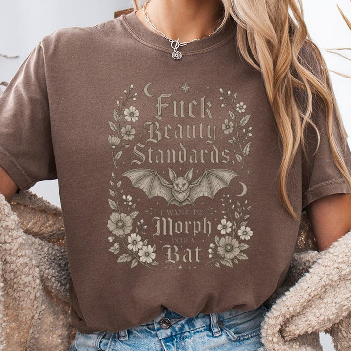 Brown t-shirt with bat, moon, and flowers graphic reading "Fuck Beauty Standards I Want to Morph into a Bat".