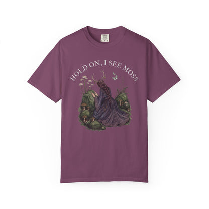 Purple t-shirt with "Hold On, I See Moss" graphic of a woman in a forest.